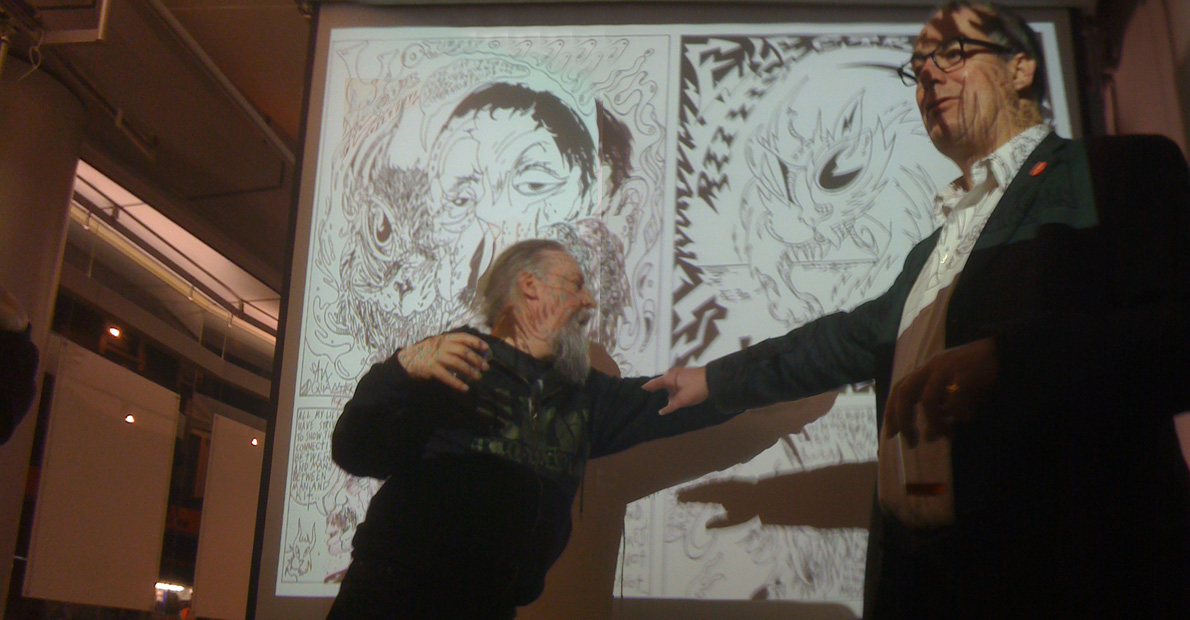 Savage Pencil and David Quantick in front of pages from their comic about Louis Wain in Dodgem Logic #7